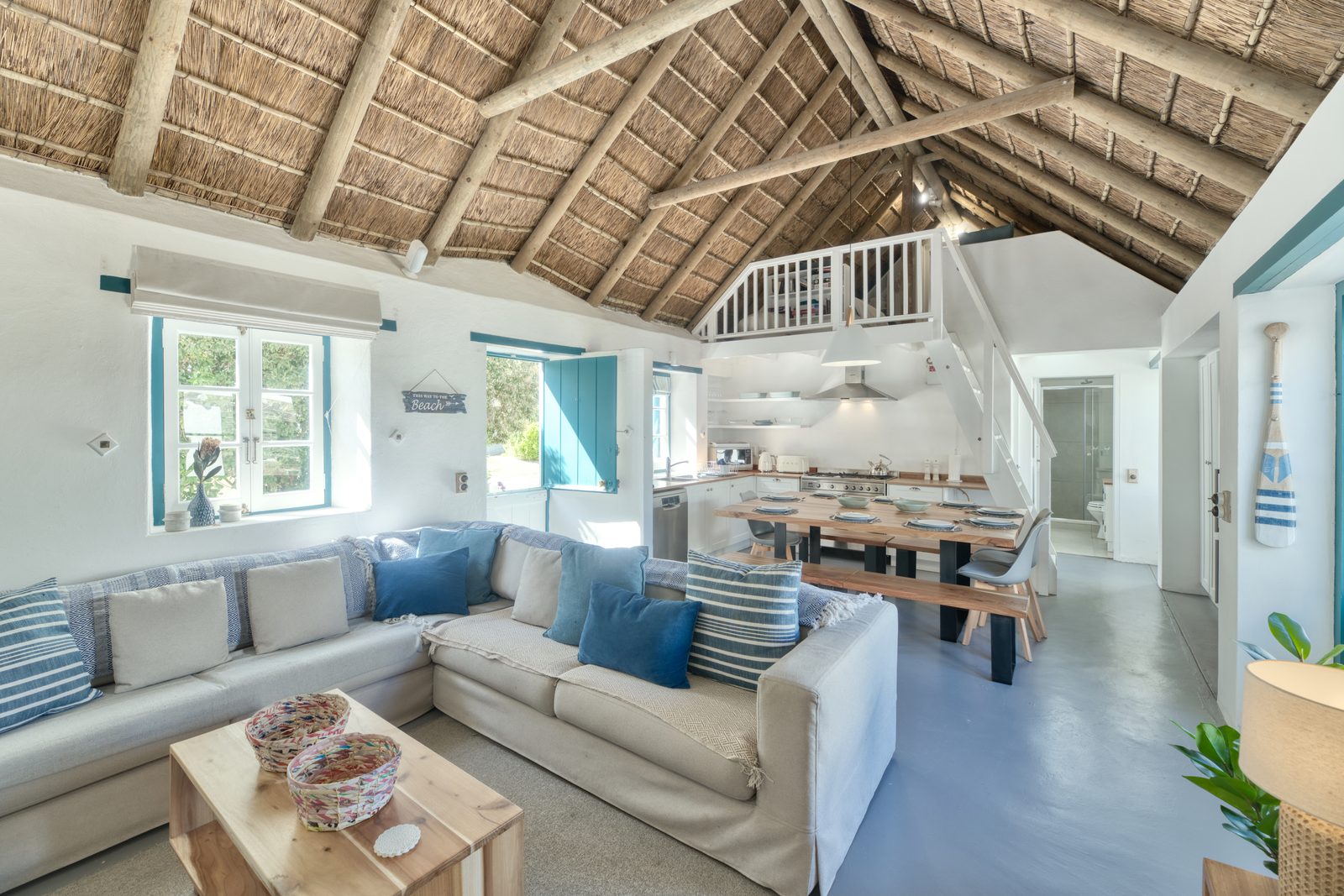 The open-plan lounge at Cape Creek Retreat, the sofa and the long dining table beneath the thatched roof