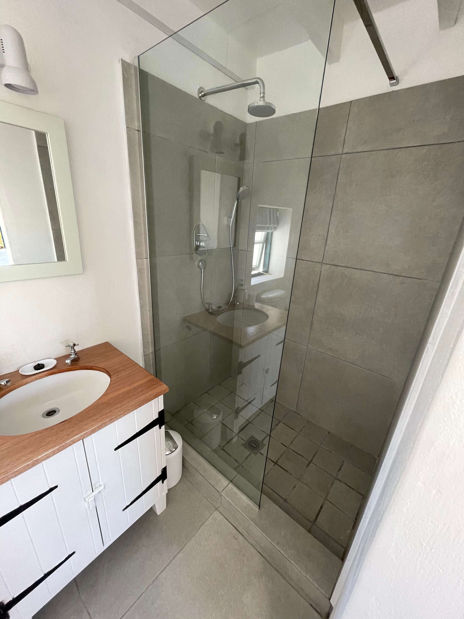 The private ensuite in Oceanbreeze Cottage, its walk-in shower behind a fixed glass screen beside the timber-topped vanity